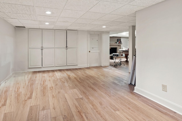 interior space featuring light wood-type flooring, a brick fireplace, and a drop ceiling