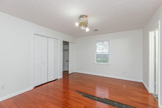 unfurnished bedroom with multiple closets, hardwood / wood-style floors, and a textured ceiling