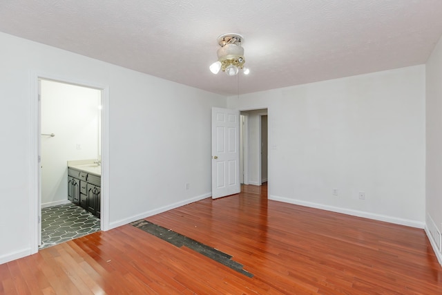 unfurnished bedroom with a textured ceiling, ensuite bath, and hardwood / wood-style flooring