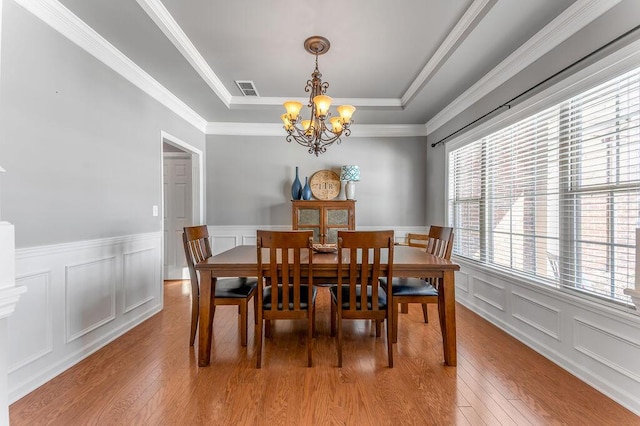 dining area featuring a chandelier, ornamental molding, light hardwood / wood-style flooring, and a tray ceiling