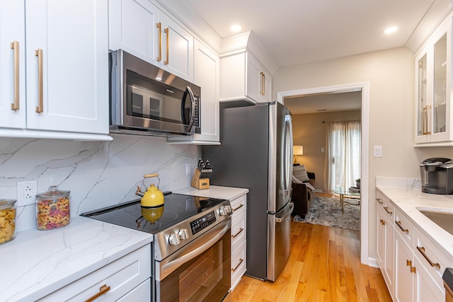 kitchen with white cabinets, backsplash, stainless steel appliances, and light hardwood / wood-style floors