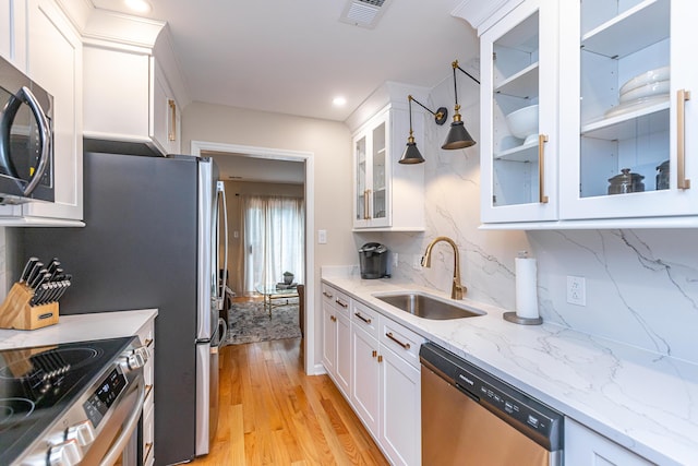 kitchen with appliances with stainless steel finishes, decorative backsplash, hanging light fixtures, white cabinets, and sink