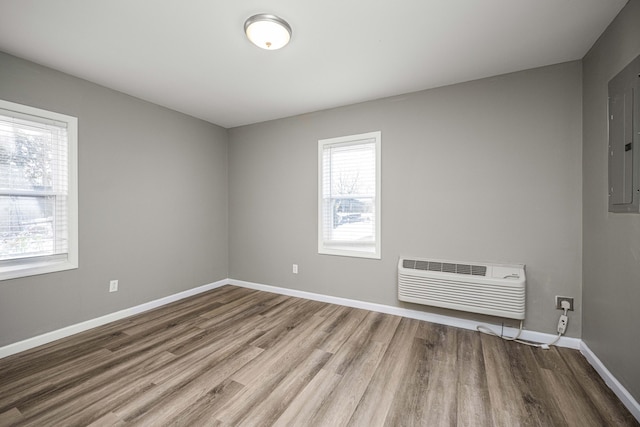 unfurnished room with wood-type flooring, a wall mounted AC, and electric panel