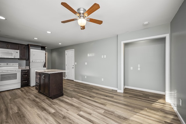 kitchen with white appliances, dark brown cabinetry, stacked washing maching and dryer, and a kitchen island