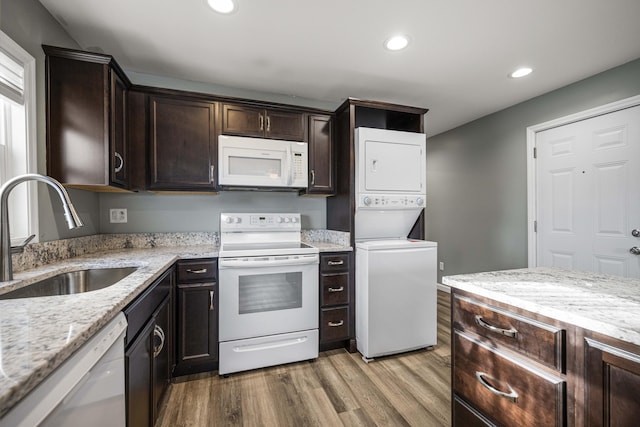 kitchen featuring dark brown cabinetry, sink, light stone counters, white appliances, and stacked washing maching and dryer