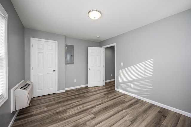 unfurnished bedroom with dark wood-type flooring, a wall mounted air conditioner, and electric panel