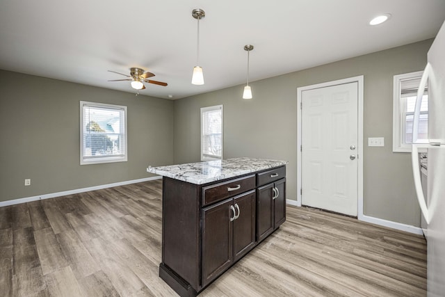 kitchen featuring light stone counters, decorative light fixtures, dark brown cabinets, white fridge, and light hardwood / wood-style floors