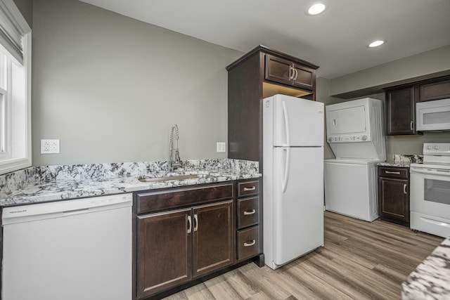 kitchen featuring sink, stacked washer / drying machine, dark brown cabinetry, white appliances, and light hardwood / wood-style flooring