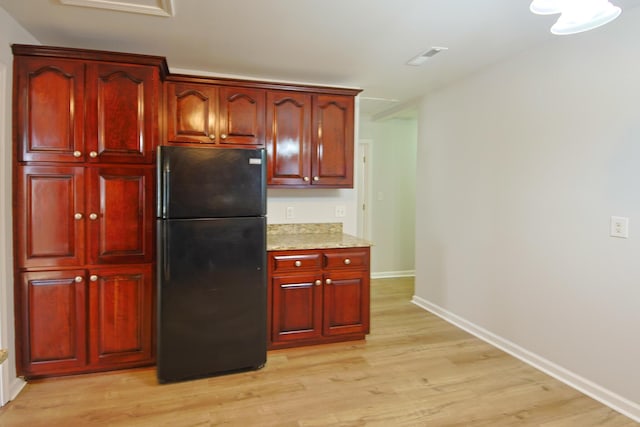 kitchen featuring black refrigerator, light wood-type flooring, and light stone countertops