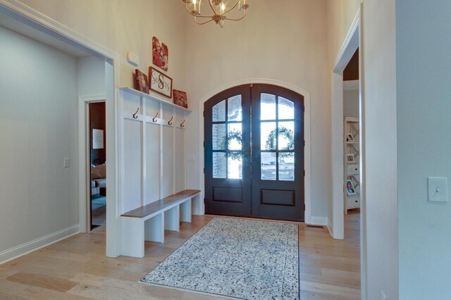 mudroom with baseboards, light wood-style flooring, arched walkways, french doors, and a chandelier