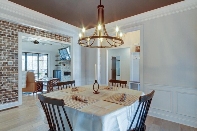 dining area with brick wall, a fireplace, wainscoting, crown molding, and light wood-type flooring