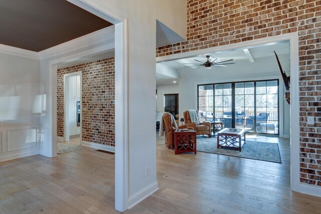 living room with brick wall, baseboards, ornamental molding, hardwood / wood-style flooring, and a ceiling fan