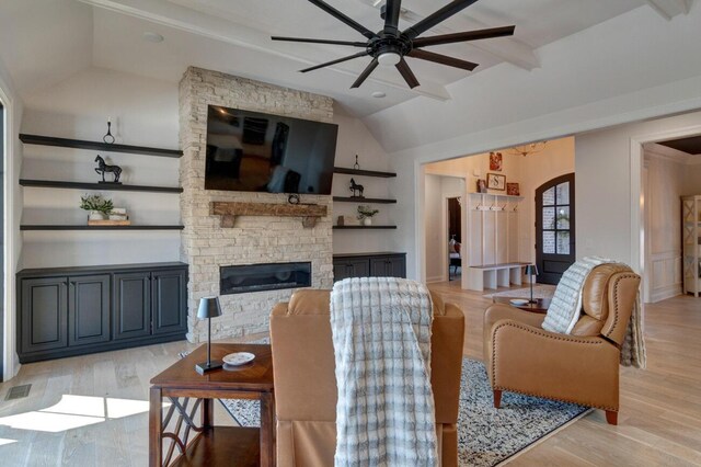 living room with visible vents, light wood-type flooring, a ceiling fan, a stone fireplace, and vaulted ceiling