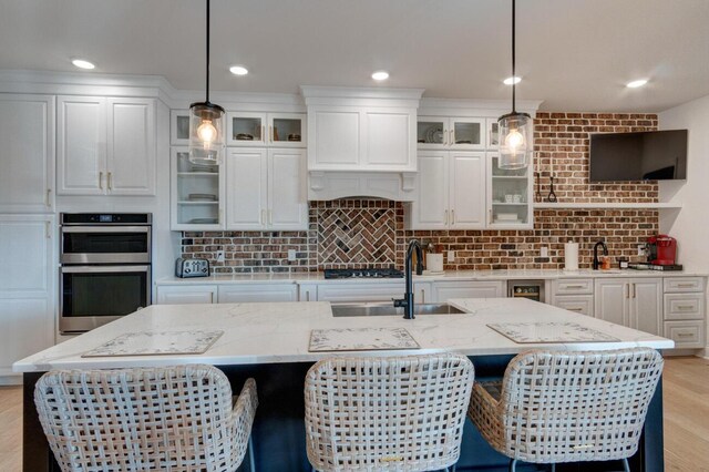 kitchen featuring light wood-type flooring, a sink, backsplash, white cabinetry, and appliances with stainless steel finishes