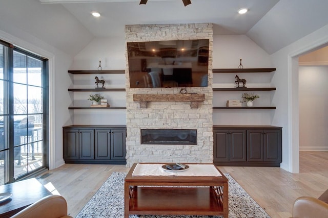 living area featuring baseboards, lofted ceiling, a stone fireplace, light wood-style flooring, and a ceiling fan