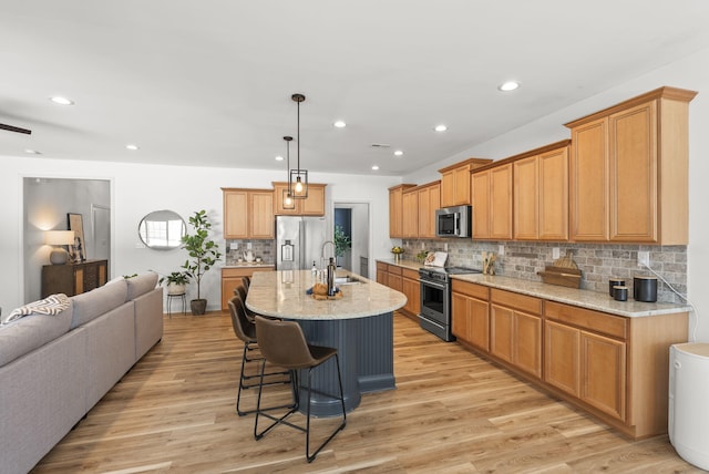 kitchen with light hardwood / wood-style floors, a center island with sink, a breakfast bar, hanging light fixtures, and stainless steel appliances