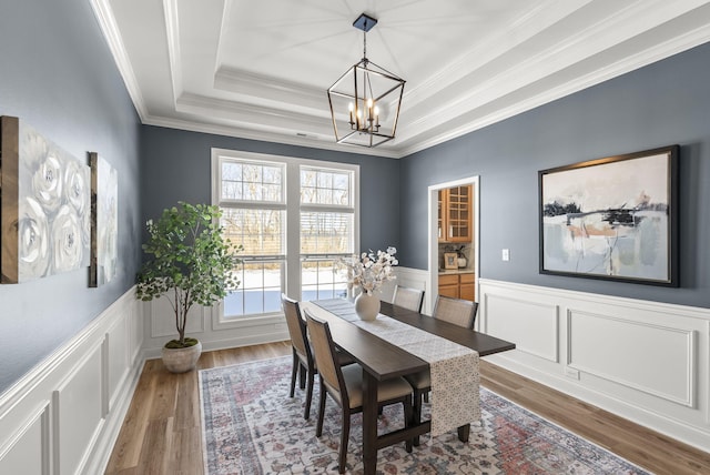 dining area with ornamental molding, a chandelier, hardwood / wood-style flooring, and a tray ceiling