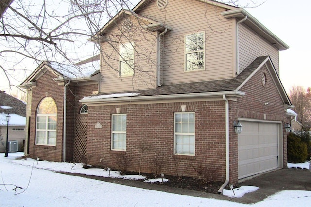 view of snowy exterior with central AC and a garage