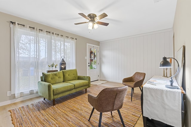 living room featuring ceiling fan, light hardwood / wood-style floors, and wooden walls