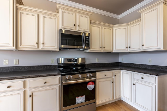 kitchen with appliances with stainless steel finishes, light hardwood / wood-style flooring, ornamental molding, and cream cabinetry