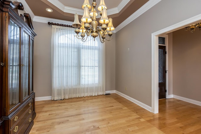 unfurnished dining area with light wood-type flooring, ornamental molding, an inviting chandelier, and a tray ceiling