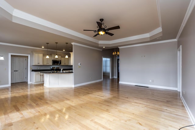 unfurnished living room with ceiling fan with notable chandelier, crown molding, light hardwood / wood-style floors, and a tray ceiling