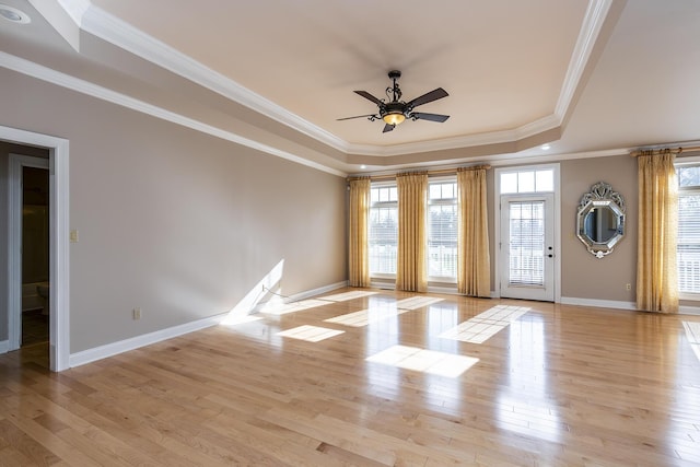 spare room with light wood-type flooring, ceiling fan, a raised ceiling, and ornamental molding