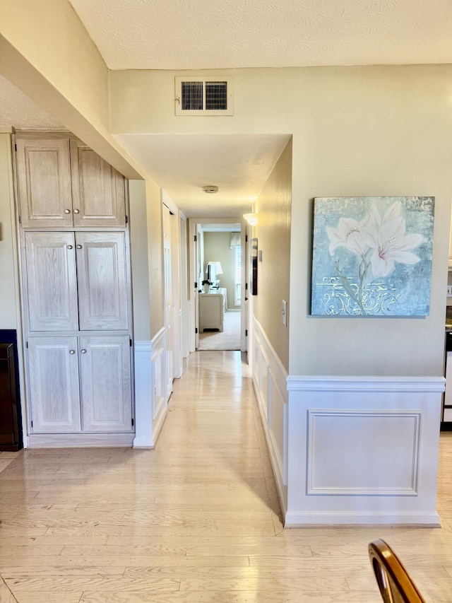 corridor with a textured ceiling and light hardwood / wood-style flooring