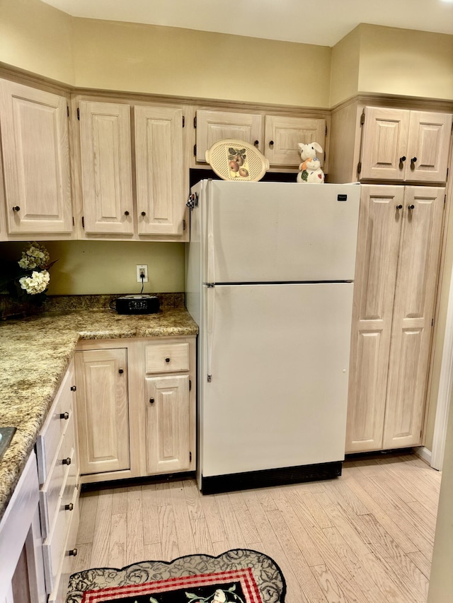 kitchen with white fridge, light stone counters, and light wood-type flooring