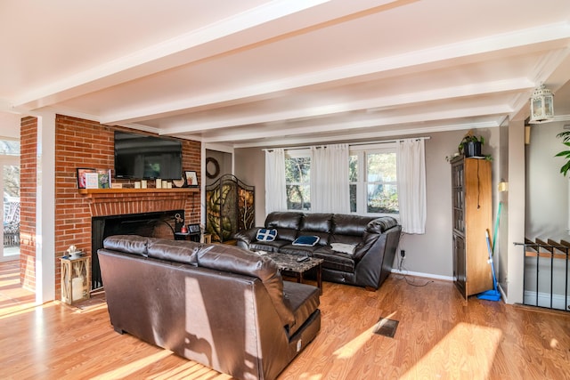 living room featuring beamed ceiling, a brick fireplace, and light wood-type flooring