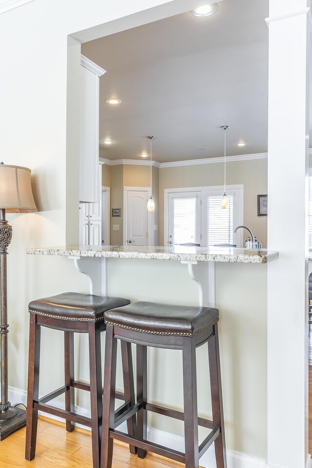 kitchen featuring a breakfast bar, light stone counters, hanging light fixtures, ornamental molding, and kitchen peninsula