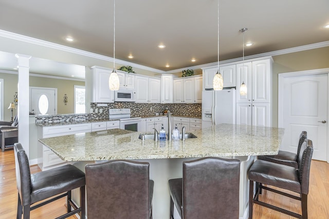 kitchen with white appliances, a breakfast bar, sink, and white cabinets