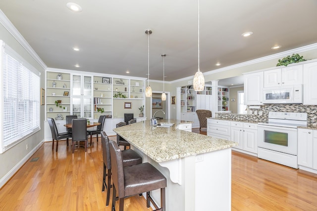 kitchen with sink, white appliances, white cabinets, a center island with sink, and decorative light fixtures