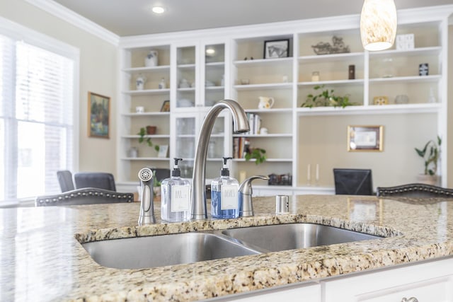 interior details with sink, hanging light fixtures, light stone counters, ornamental molding, and white cabinets