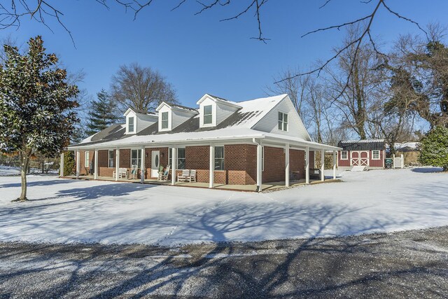 view of snow covered exterior featuring a storage shed and covered porch