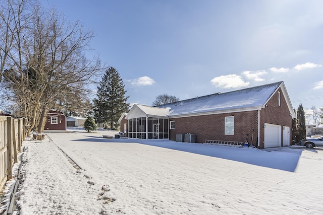 snow covered property featuring a garage, a sunroom, and central AC