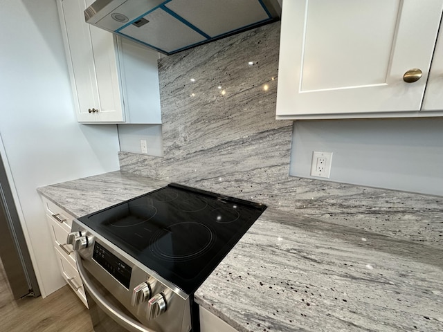 kitchen featuring light stone countertops, stainless steel range with electric cooktop, white cabinetry, tasteful backsplash, and range hood