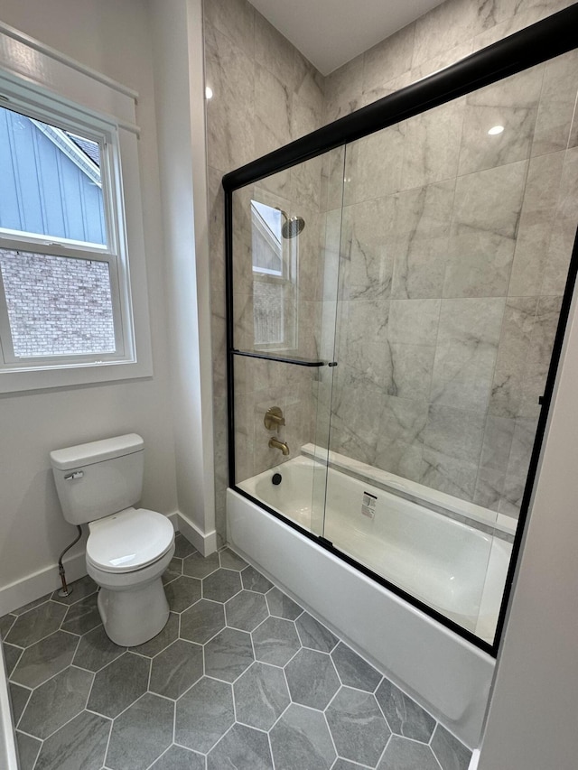 bathroom featuring toilet and shower / bath combination with glass door