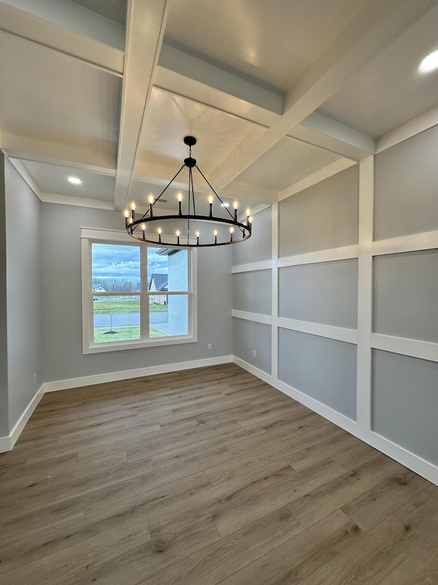 unfurnished dining area with beam ceiling, wood-type flooring, an inviting chandelier, and coffered ceiling