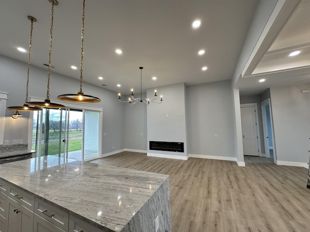 kitchen featuring a spacious island, decorative light fixtures, an inviting chandelier, light wood-type flooring, and light stone counters