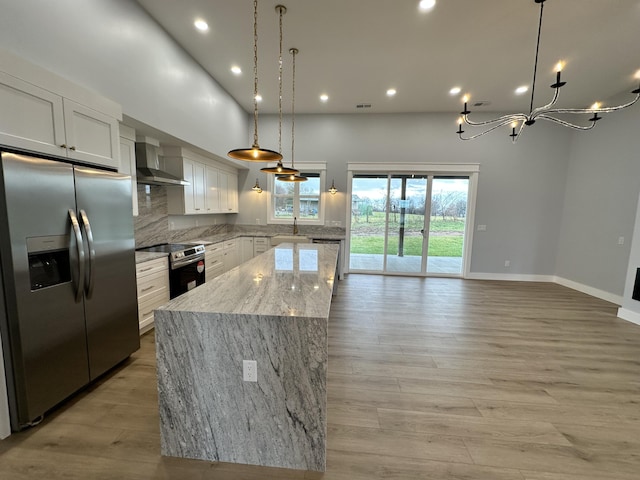 kitchen with appliances with stainless steel finishes, wall chimney exhaust hood, white cabinets, and hanging light fixtures