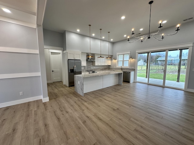 kitchen featuring a large island, stainless steel appliances, wall chimney exhaust hood, pendant lighting, and white cabinets