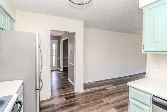 kitchen with dark wood-type flooring, appliances with stainless steel finishes, green cabinets, and a textured ceiling