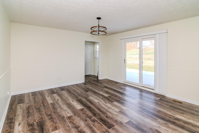 empty room featuring dark hardwood / wood-style flooring, a notable chandelier, and a textured ceiling