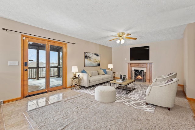 tiled living area with a lit fireplace, baseboards, ceiling fan, and a textured ceiling