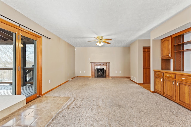 unfurnished living room featuring light colored carpet, visible vents, a fireplace with flush hearth, a textured ceiling, and baseboards