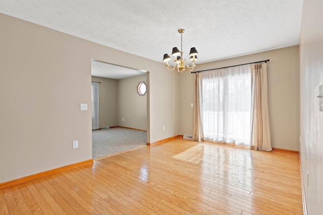 empty room with a chandelier, a textured ceiling, baseboards, and hardwood / wood-style flooring