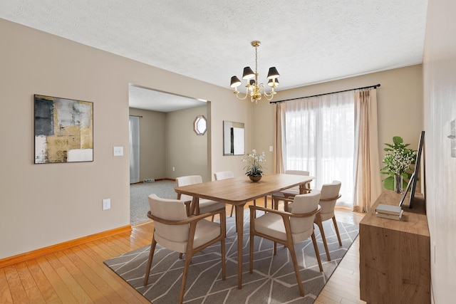 dining space featuring an inviting chandelier, a textured ceiling, baseboards, and hardwood / wood-style floors