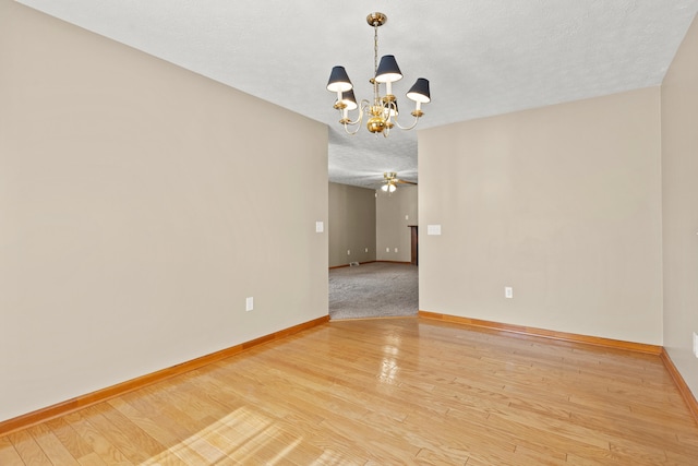 empty room with a chandelier, a textured ceiling, light wood-type flooring, and baseboards