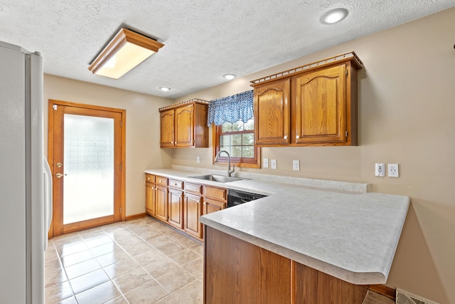 kitchen featuring visible vents, freestanding refrigerator, a peninsula, light countertops, and a sink